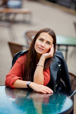 Deri ceketli, uzun saçlı esmer masada oturuyor.