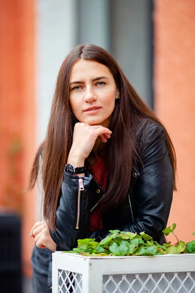 Eski bir binanın arka planında deri ceketli, uzun saçlı esmer.