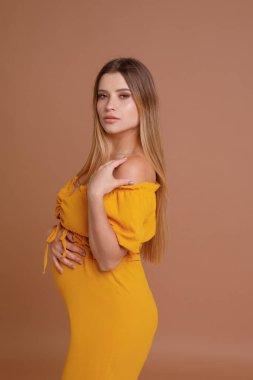 Bej arka planda stüdyoda hamile bir kadın var.