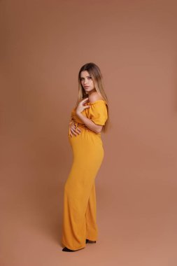 Bej arka planda stüdyoda hamile bir kadın var.