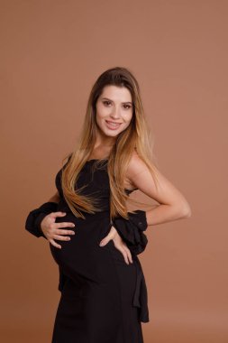 Bej arka planda stüdyoda hamile bir kadın var.