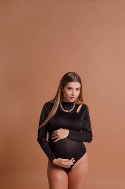 Bej arka planda stüdyoda hamile bir kadın var.