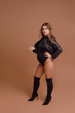 Bej arka planda stüdyoda hamile bir kadın var.