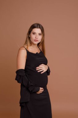 Bej arka planda stüdyoda hamile bir kadın var.