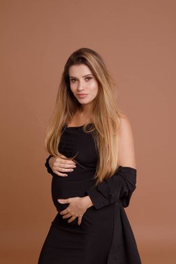 Bej arka planda stüdyoda hamile bir kadın var.