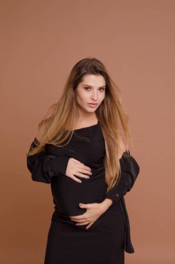 Bej arka planda stüdyoda hamile bir kadın var.