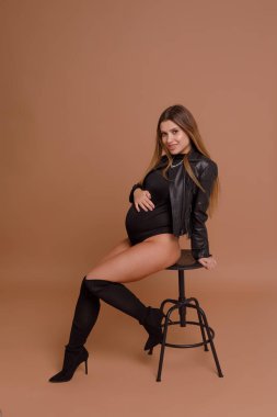 Bej arka planda stüdyoda hamile bir kadın var.