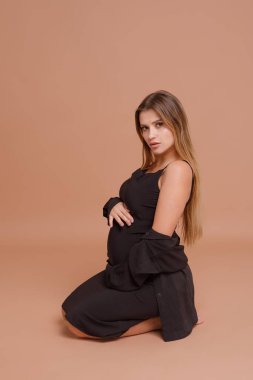 Bej arka planda stüdyoda hamile bir kadın var.