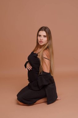 Bej arka planda stüdyoda hamile bir kadın var.