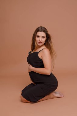 Bej arka planda stüdyoda hamile bir kadın var.