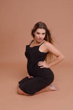 Bej arka planda stüdyoda hamile bir kadın var.