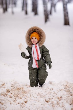 Sıcak kış giysileri içindeki küçük çocuk kışın parkta tulum giyer.