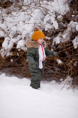Sıcak kış giysileri içindeki küçük çocuk kışın parkta tulum giyer.