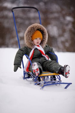 Sıcak kış giysileri içindeki küçük çocuk kışın parkta tulum giyer.