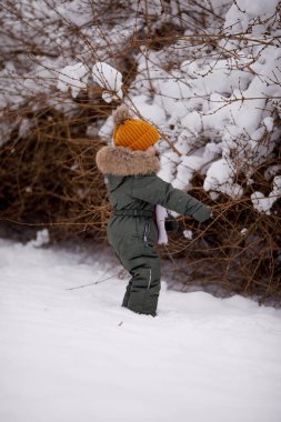 Sıcak kış giysileri içindeki küçük çocuk kışın parkta tulum giyer.