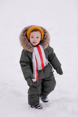 Sıcak kış giysileri içindeki küçük çocuk kışın parkta tulum giyer.