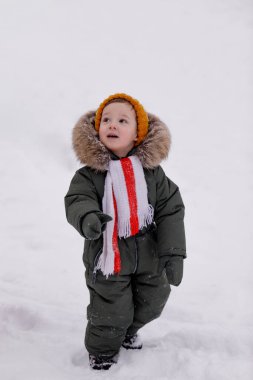 Sıcak kış giysileri içindeki küçük çocuk kışın parkta tulum giyer.