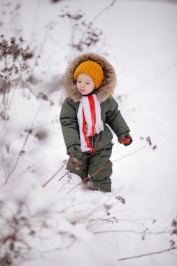 Sıcak kış giysileri içindeki küçük çocuk kışın parkta tulum giyer.