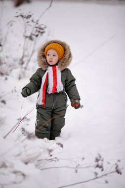 Sıcak kış giysileri içindeki küçük çocuk kışın parkta tulum giyer.