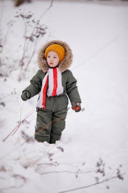 Sıcak kış giysileri içindeki küçük çocuk kışın parkta tulum giyer.