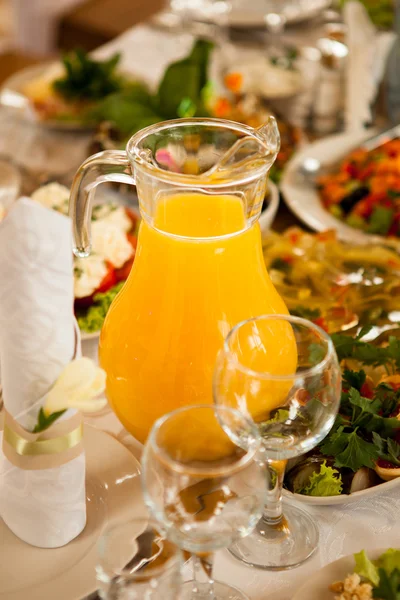 Jug of orange juice in the center of the holiday table with food — Stock Photo, Image