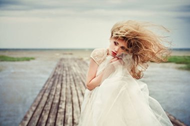 Deniz rıhtımında rüzgarda uçan saçları olan gelinlikli güzel bir kızın portresi..
