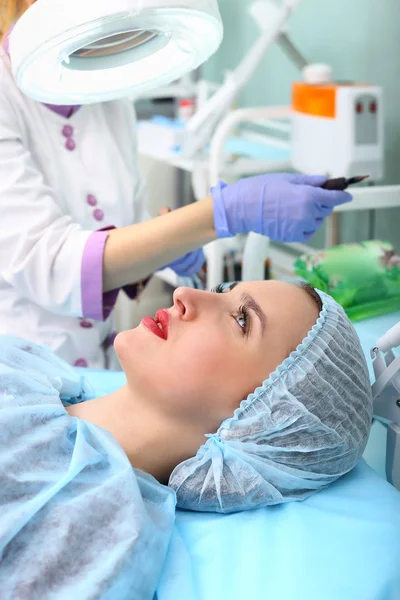 Kosmetikerin schminkt das Gesicht einer Frau dauerhaft — Stockfoto