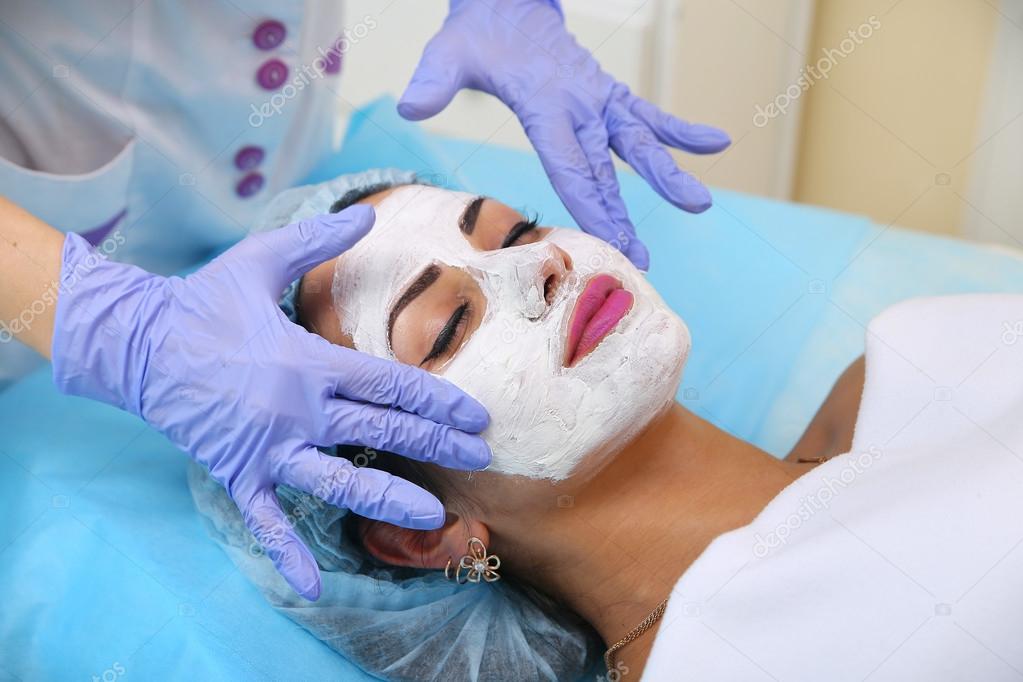 Doctor beautician applies a clay mask on face hands beautiful wo