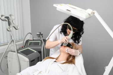 Woman having facial hair removal laser. clipart