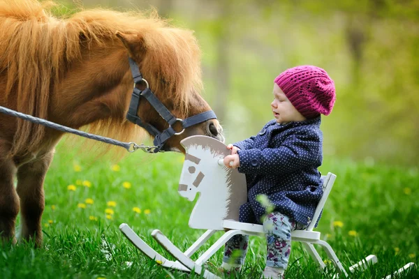 Babymeisje op houten rocking paard en pony — Stockfoto