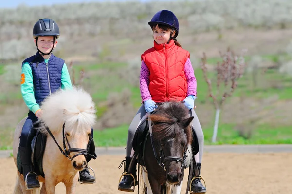 Niño y niña montando un pony — Foto de Stock