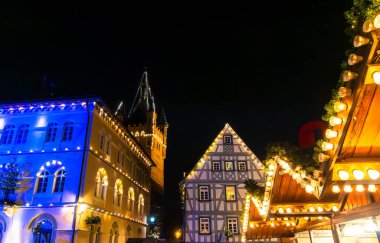 Almanya 'nın Bad-Wimpfen şehrinde canlı bir Noel sahnesi. Taş ve kereste binalarında mavi ve sıcak ışıklar, şenlikli bir atmosfer için fener ışığında tatil tezgahları.