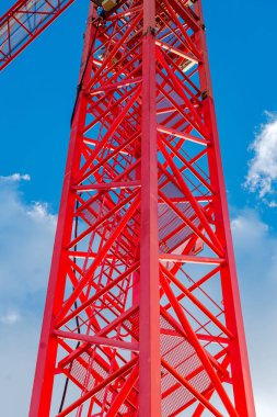 Düşük açı açısı parlak kırmızı bir vinç yapısına bakıyor ve açık mavi gökyüzüne karşı duruyor.