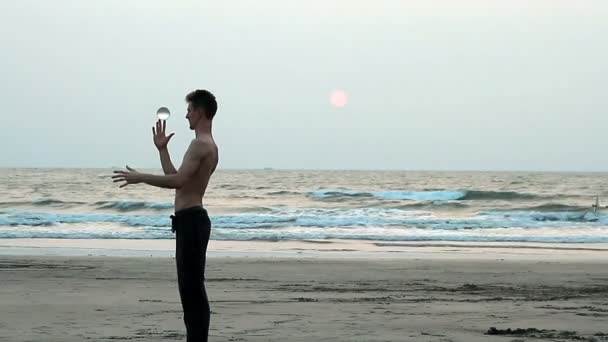 Неизвестный жонглирует стеклянным мячом на пляже — стоковое видео