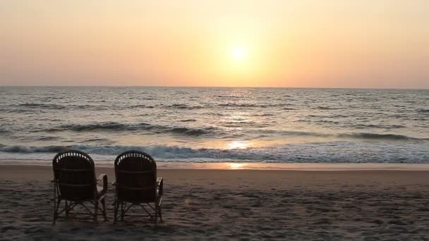 Два стула возле береговой линии на закате — стоковое видео