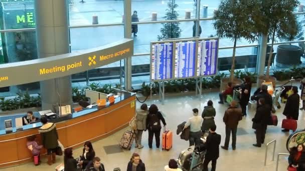 Människor nära informationstavla inne i ankomsthallen på flygplatsen Domodedovo — Stockvideo
