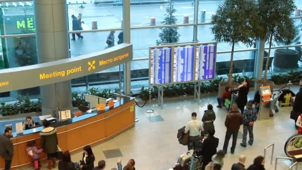 Personnes à proximité du panneau d'information à l'intérieur hall d'arrivée à l'aéroport international Domodedovo — Video