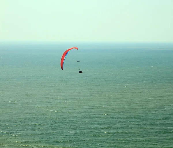 Red paraglider flying in blue sky over the ocean. — Stock Photo, Image