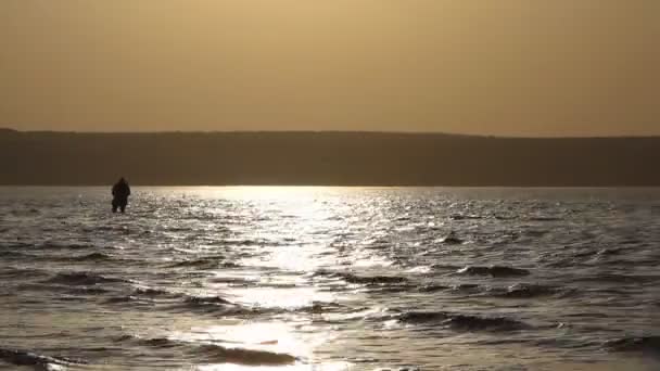 Человек рыбачит в озере на закате — стоковое видео