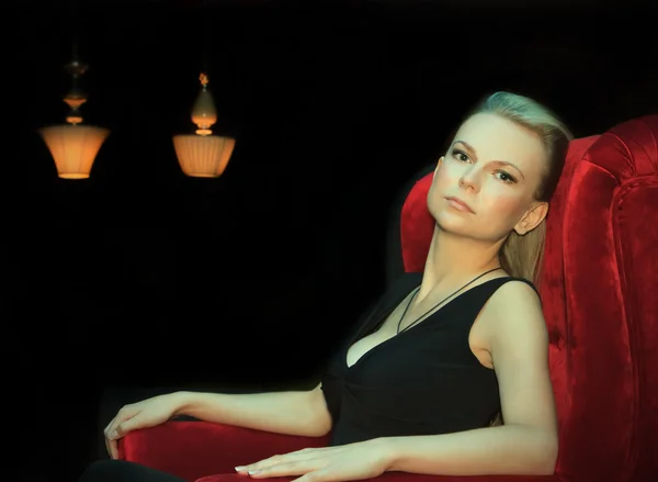 Kobieta siedzi w czerwone krzesło w ciemności — Zdjęcie stockowe