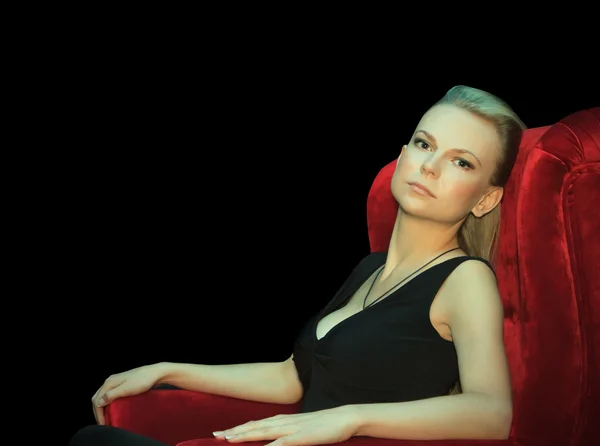 Piękna kobieta siedzi w czerwone krzesło w ciemności — Zdjęcie stockowe