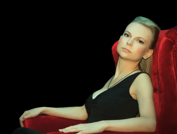 Beautiful female sitting in red chair at the darkness — Stock Photo, Image