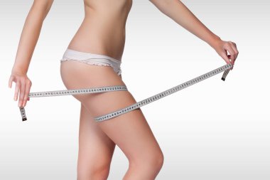 Gri arkaplanlı bir arkaplanda bant ölçüsü kullanan bir kadın.