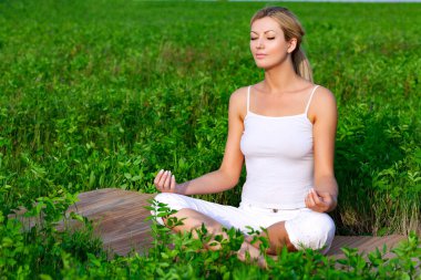 Dışarıda yoga pozisyonunda oturan güzel bir kadın. Gözleri kapalı. 