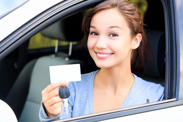 Menina em um carro mostrando uma chave e um cartão branco vazio — Fotografia de Stock