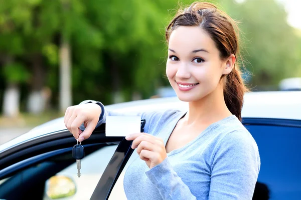 Woman stands beside a car and shows keys and white card — Stock Photo, Image