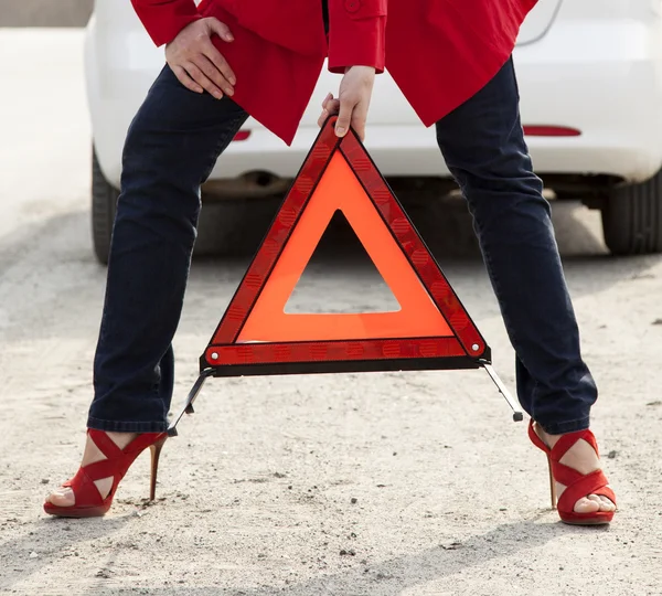 Woman with a red triangle sign on a road — Stock Photo, Image