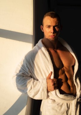 Beyaz bornoz giyen kaslı genç adam.