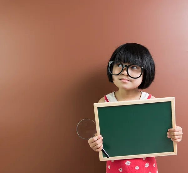 Παιδί της Ασίας σχολείο κρατήστε ένα μαυροπίνακα και Μεγεθυντικός φακός — Φωτογραφία Αρχείου