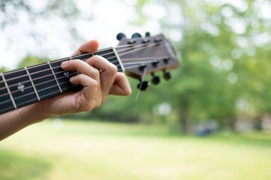 Gitar akoru arka planda ağaçlar olan bir parkta çalıyordu.